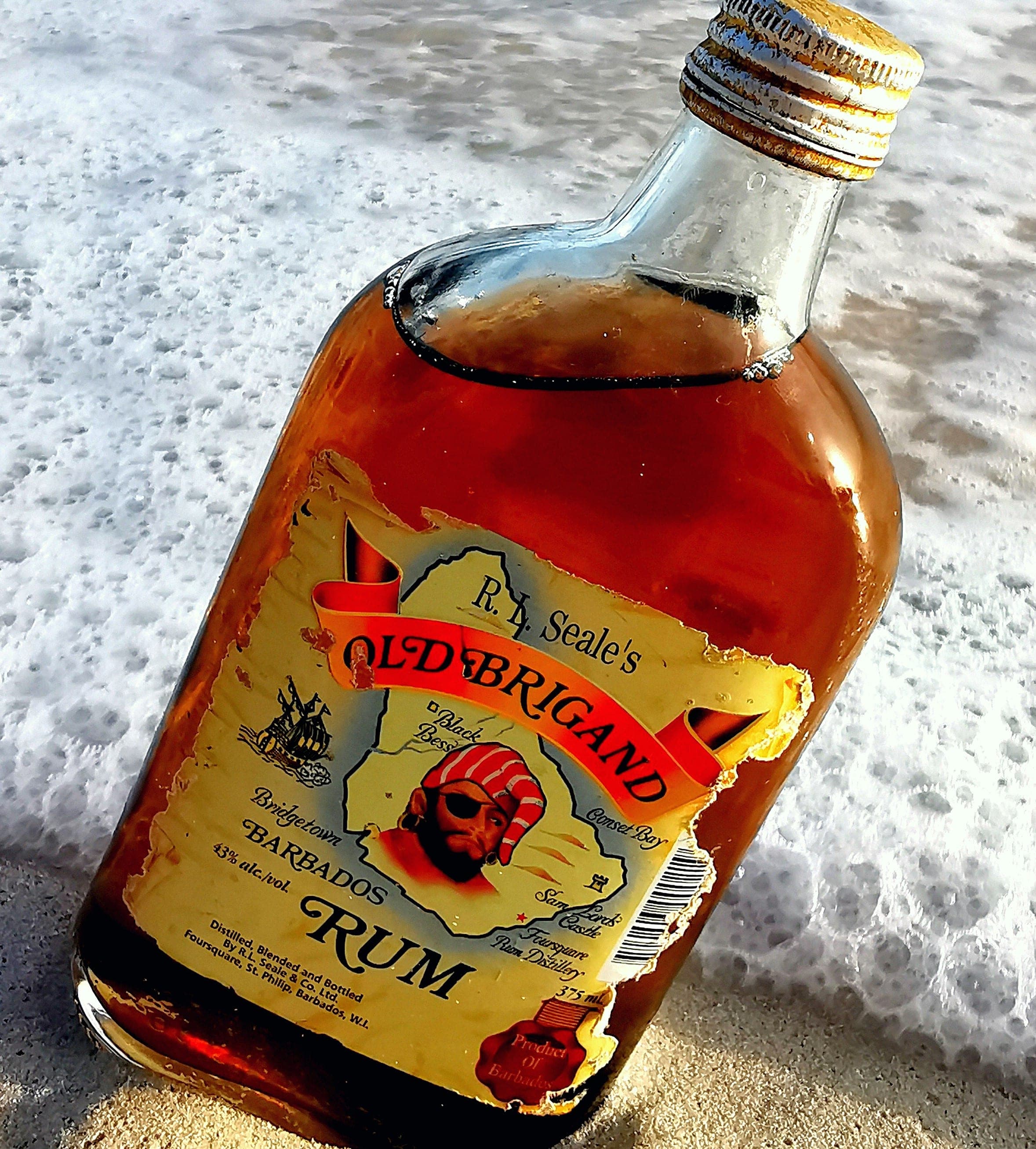 Бутылка барбадосского рома Old Brigand на мокром песке у кромки набегающей волны